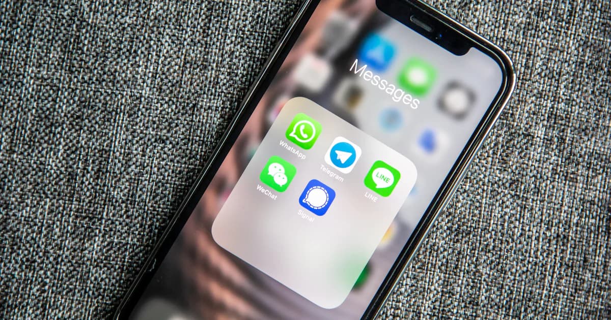 Smartphone showing a folder of messaging apps including WhatsApp on a fabric surface